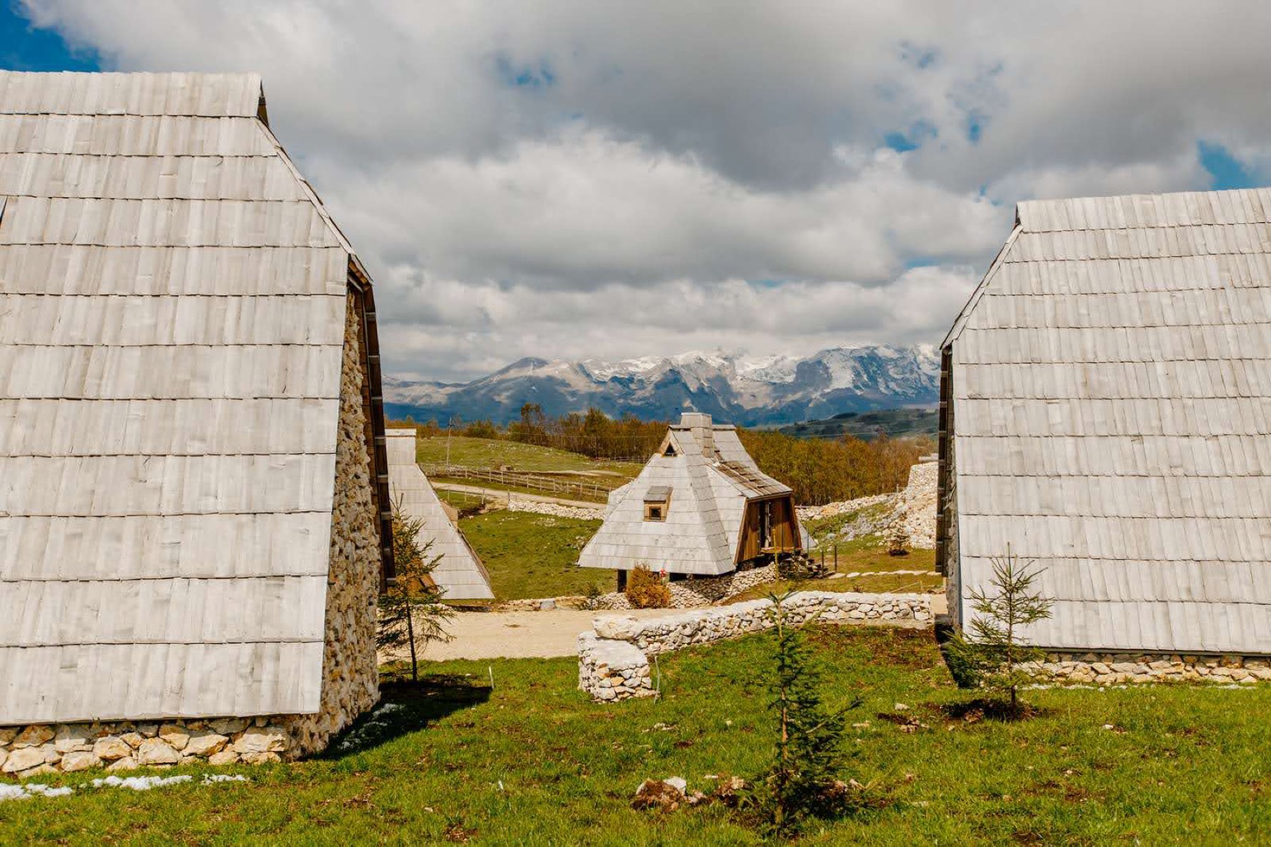 Shingle-roofed stone houses of Etno Selo Vojinović beneath the snow-capped Durmitor massif
