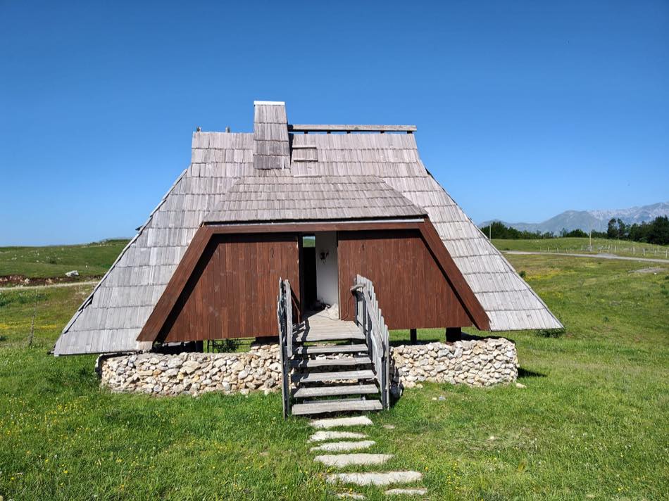 Finished guest house — shingle roof and timber gable on a dry-stone base