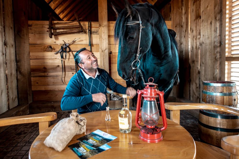 Željko Vojinović at a timber table in the village, sharing rakija with his black horse at his shoulder